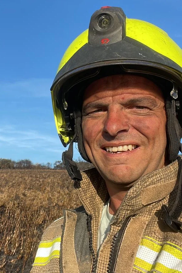 Graham Murt in fire kit and helmet, standing in a burnt-out field at a wildfire in Cornwall
